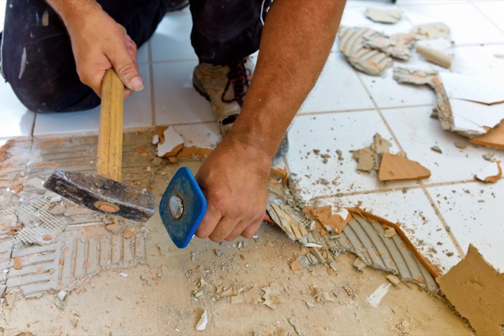 Cómo planificar una reforma integral paso a paso Operario retirando azulejos con martillo y cincel en una reforma de baño